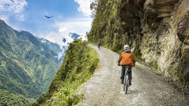 Waghalsige Radfahrer auf dem Weg in die Yungas. Im Hintergrund kreist ein Kondor über dem Tal.