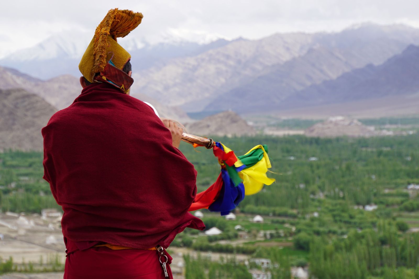 Mönch bläst die Puja auf dem Dach des Klosters von Tikse