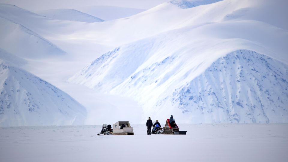 Mit Schneemobilen an der Eiskante vor mächtiger Bergulisse auf Baffin Island