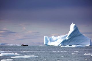 Ein Schlauchboot nähert sich einem riesigen Eisberg