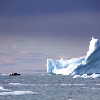 Ein Schlauchboot nähert sich einem riesigen Eisberg