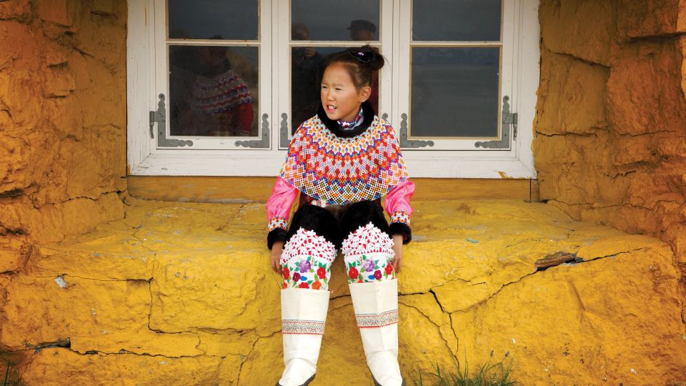 Junge Inuit in traditioneller Kleidung vor einem Haus