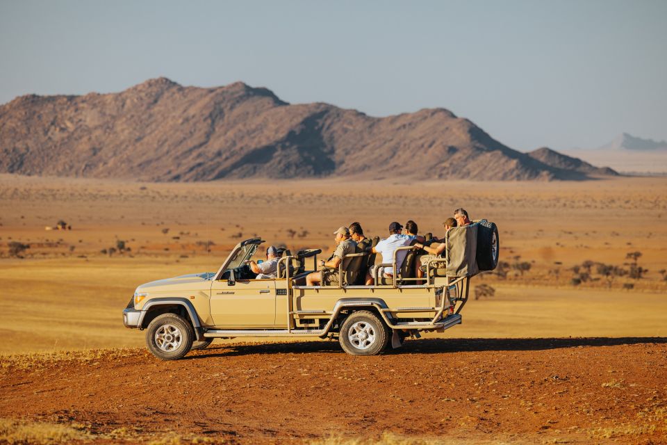 Safarifahrzeug mit Gästen in der Wüstenlandschaft von Namibia