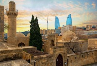 Blick auf die historischen Moscheen und die Mauern des Shirvanshahs Palastes in der Altstadt und moderne gläserne Flower Towers Wolkenkratzer im dramatischen Licht des Sonnenuntergangs