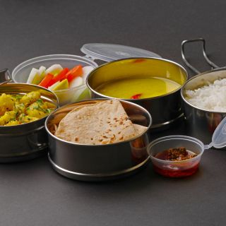 Typische Edelstahl-Lunchbox oder Tiffin mit Maharashtrian-Speisen Chapati oder Roti, Dal – ein Linsengericht, weißer Reis, Kartoffel-Sabji mit Salat und Gurke.