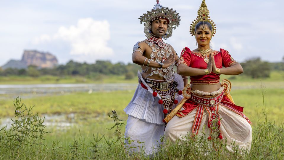 Tänzer in traditioneller Kleidung mit Sigiriya Löwenfelsen im Hintergrund.